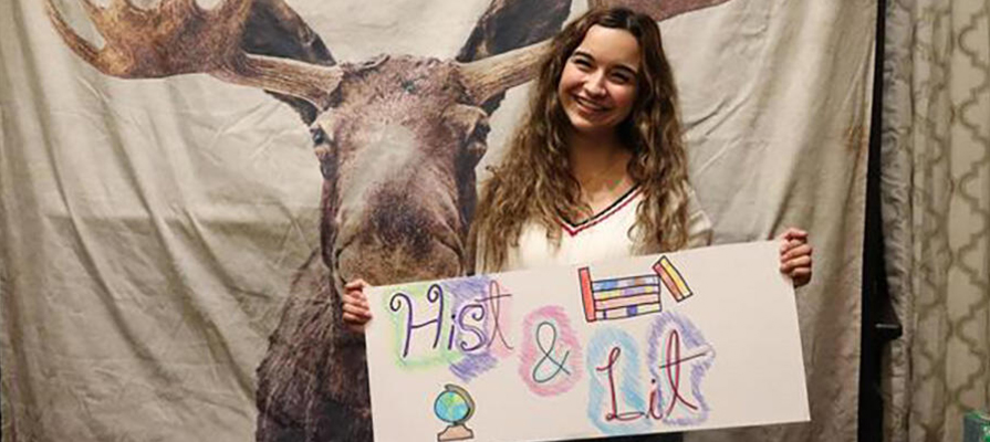 Student holding sign in front of moose banner