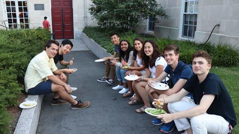 students sitting on steps in courtyard with BBQ food